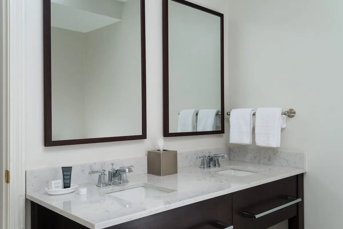 A bright, modern bathroom with double sinks, large mirrors, a marble countertop, and neatly folded towels. The space feels fresh and inviting, ideal for self-care routines and relaxation.