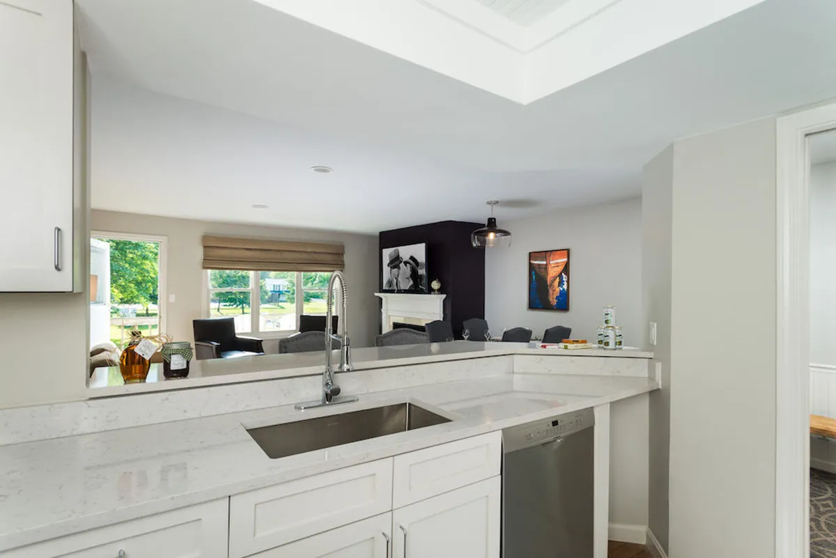 A modern kitchen features a sleek countertop and sink, with views into the comfortable living area through a wide opening. Artwork and contemporary decor add warmth, while the open design makes it easy to move between cooking, socializing, and relaxing.