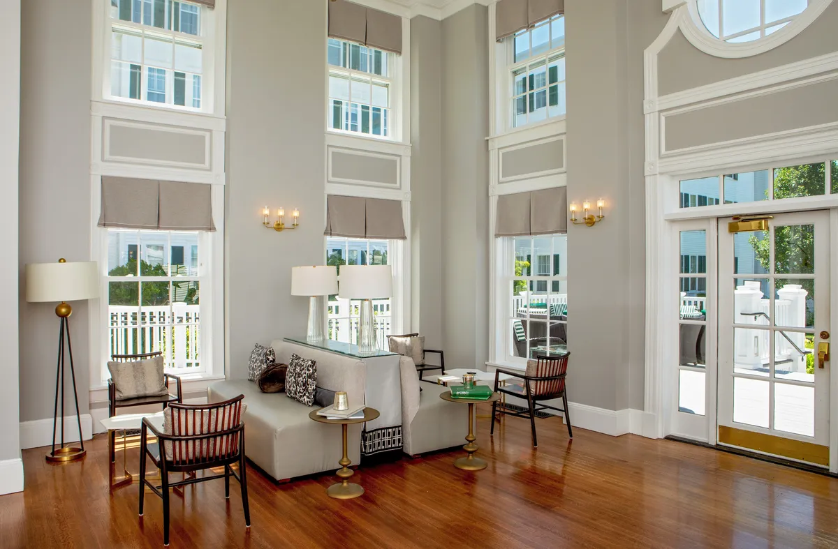 A bright and airy living room with large windows letting in ample natural light, stylish seating grouped around a central table, and a lamp adding a cozy touch. The atmosphere is calm and sophisticated, perfect for socializing, relaxing after outdoor excursions, or enjoying a sunny Vermont afternoon.