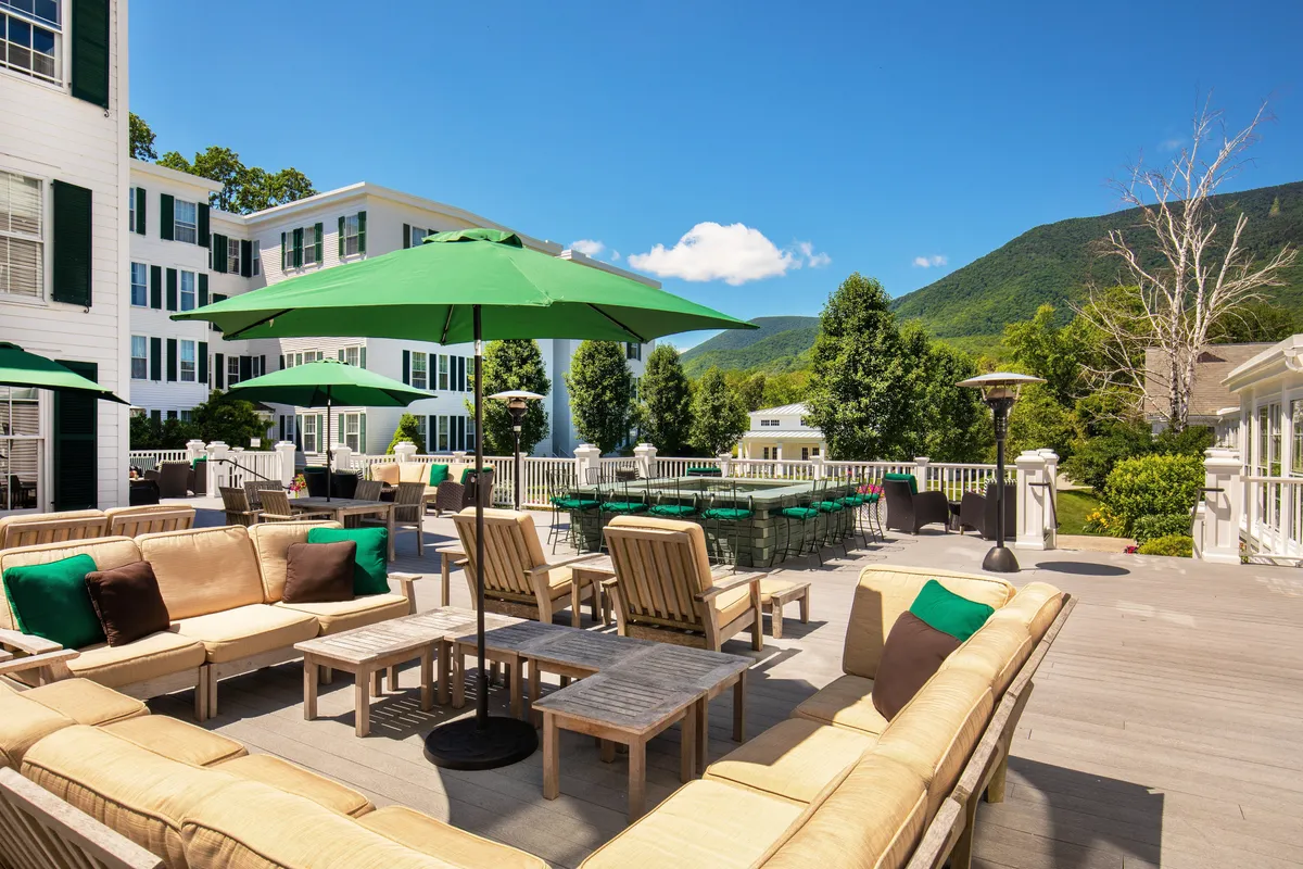 An outdoor seating area with green umbrellas and comfortable chairs, set against the backdrop of distant mountains. The space is perfect for relaxing, socializing, or enjoying outdoor dining, and transitions beautifully from day to night activities.